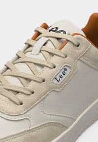 Κοντινό πλάνο μπεζ αθλητικού παπουτσιού Lee με υφασμάτινα κορδόνια, τμήματα από σουέντ και αντίθετη καφέ εσωτερική επένδυση.