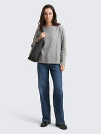 Maglione in lana grigia, jeans blu, borsa in pelle nera. Il maglione ha una scollatura rotonda, vestibilità ampia; i jeans sono a taglio diritto. Dettaglio lavorato a maglia strutturata.