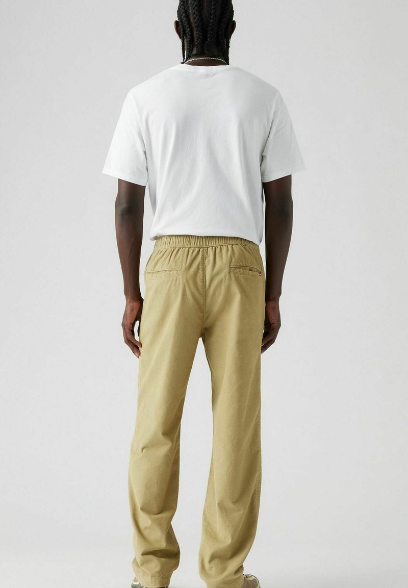 Conjunto informal que incluye una camiseta blanca básica y pantalones elásticos de talle alto en beige claro con bolsillos traseros. Tela de algodón suave, corte relajado.