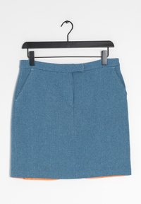 Mini falda texturizada azul con bolsillos laterales colgando de una percha negra, con un forro naranja ligeramente visible en el dobladillo inferior.