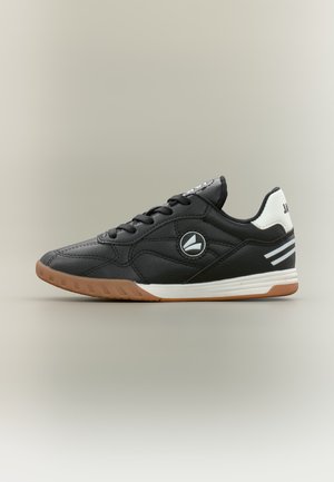 Zwarte lage sneaker met zwarte veters, witte hieltab, witte zoolaccenten en lichtbruine loopzool, zijaanzicht op een neutrale achtergrond.
