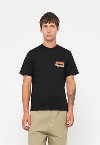 Sort bomuld t-shirt med rund hals og korte ærmer. Har orange grafisk tekst på venstre brystområde. Traditionel pasform, glat tekstur.