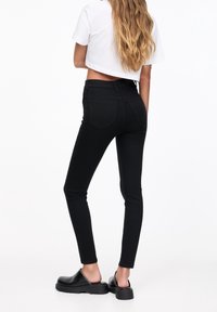 Jeans skinny negros con cintura alta, de textura suave, con dos bolsillos traseros, combinados con unos zapatos negros sin cordones.