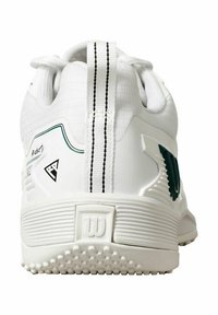 Zapatilla deportiva blanca con parte superior texturizada, cuello acolchado y acentos en verde y negro. Suela de goma con un patrón antideslizante.