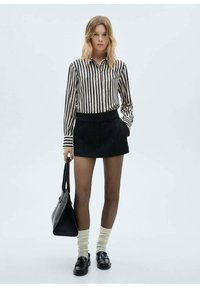 Zwart-wit gestreepte overhemd met knopen, hoge zwarte shorts, zwarte tas, crèmekleurige knielange sokken en zwarte loafers. Glad oppervlak, op maat gemaakt.