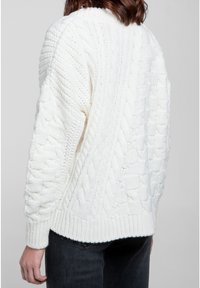 Vit kabelstickad tröja med strukturerade mönster och ribbad nederkant. Designen inkluderar överdimensionerade ärmar och en avslappnad passform.