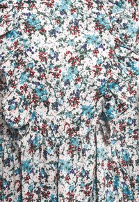 Bloemendress met gerimpelde accenten. Witte achtergrond met blauwe, rode en groene bloemen. Lichtgewicht stof met geplooide details.