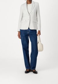 Ljust grå skräddarsydd kavaj med två knappar, matchad med blå vida jeans. Svarta platta skor och en krämfärgad handväska fulländar outfiten.