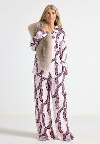 Set di pigiami rosa a fantasia con un design di foglie in borgogna scuro, con vestibilità ampia e texture morbida. Un cappotto in pelliccia sintetica è appoggiato su una spalla.