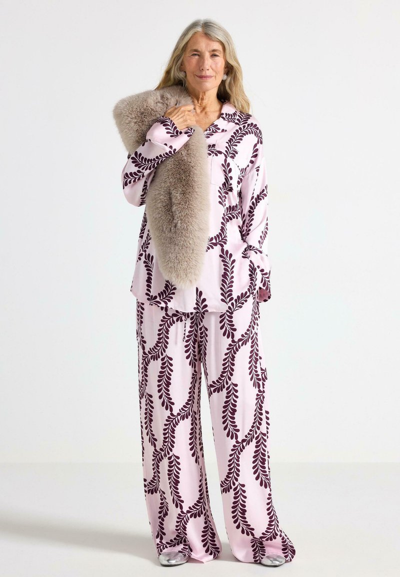 Set di pigiami rosa a fantasia con un design di foglie in borgogna scuro, con vestibilità ampia e texture morbida. Un cappotto in pelliccia sintetica è appoggiato su una spalla.