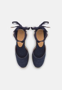Námornícke modré espadrilky s textilným zvrškom, okrúhlym špičkou a viazaním okolo členkov. Majú tkanú jutu podrážku a koženú stielku.