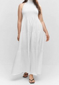 Biała maxi sukienka z dekoltem halter, warstwowym krojem i miękkim, lekkim materiałem. Noszona z czarnymi klapkami.