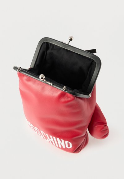 Κόκκινη δερμάτινη πορτοφολάκι για κέρματα σε σχήμα γαντιού πυγμαχίας με λευκό λογότυπο και ασημένιο μεταλλικό κλείστρο, που ανοίγει και αποκαλύπτει μαύρο εσωτερικό φόδρα.