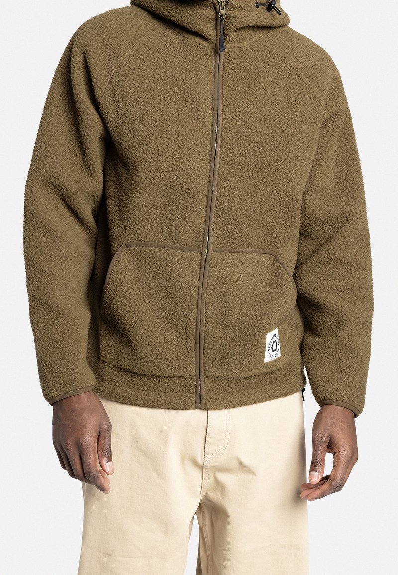 Giacca in pile marrone con chiusura a zip frontale, cappuccio e due tasche a toppa. Rifinitura in zip liscia e etichetta del logo all'orlo. Materiale morbido e testurizzato.