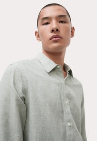 Camisa de manga larga a cuadros verde claro con collar botón y una textura sutil; cuenta con botones blancos y un ajuste relajado.