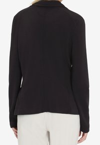 Giacca nera su misura con una texture liscia, maniche lunghe e colletto a grande punta, caratterizzata da una silhouette aderente e cuciture posteriori.