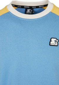 Sweat-shirt bleu avec col blanc, accents jaunes aux épaules et petite écusson du logo Starter sur la poitrine gauche.