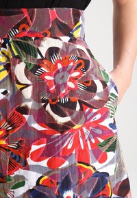 Jupe florale colorée avec des motifs audacieux rouges, violets et verts, en tissu semi-transparent, avec une taille élastique et des détails de poche latérale.