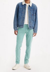 Denimjacka med shearlingkrage, i kombination med mintgröna byxor och vita sneakers. Jackan har knäppning framtill och fickor.