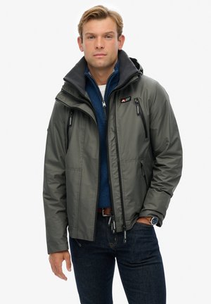 Dark grey insulated jacket with a hood, featuring zippers, a high collar, and a blue inner layer visible at the neckline.