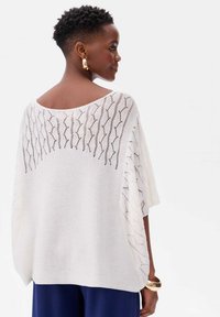 Witte gebreide poncho-stijl top met een losse pasvorm, voorzien van een textuurpatroon langs de schouders en open zijkanten. Glad stofdetail.