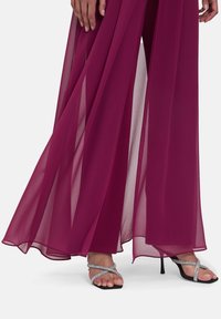 Combinaison en chiffon marron avec un design fluide et un tissu superposé. Associée à des talons noirs à lanières ornés d'accents argentés.