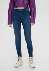 Džíny z modrého denimu s vysokým pasem a úzkým střihem, s hladkým povrchem, klasickým designem pěti kapes a jemným ombré efektem, doplněné béžovými teniskami s vysokým střihem.