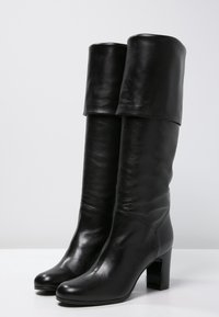 Bottes en cuir noir montantes, avec un haut replié, un bout arrondi et un talon bloc, dotées d'une texture lisse et d'une finition polie.