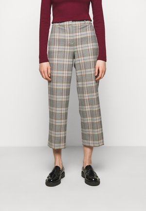 Henkilö, jolla on ylintä vyötäröä olevat cropped-harmaat ruudulliset housut yhdistettynä burgundinpunainen pitkähihaiseen toppiin ja mustiin hapsullisiin loafer-kenkiin.