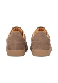 Pruunid sametkevad sneakerid, millel on kummitaldad, pehme krae ja oranž sisevooder. Seljal on tekstuuriga õmbluse detail.
