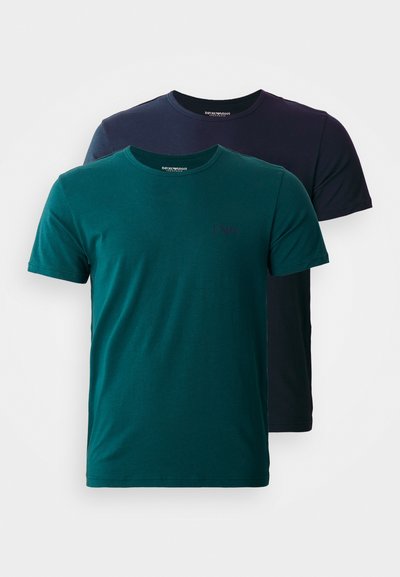 Deux t-shirts à col ras du cou, l'un teal et l'autre marine foncé, tous deux en coton, avec des manches courtes et un logo discret sur la poitrine.