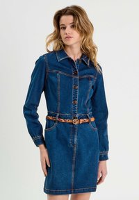 Robe en denim bleu profond avec une silhouette ajustée, fermeture à boutons sur le devant, col pointu, manches longues et une ceinture tissée beige à la taille.