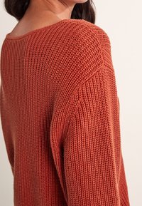 Sweter w kolorze rdzy o luźnym, teksturowanym splocie, z szerokim dekoltem i opuszczonymi ramionami, zapewniający swobodny krój.
