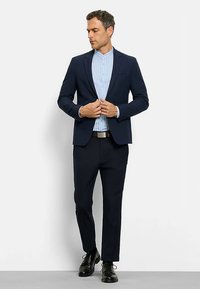 Navy suit with slim fit jacket and trousers; light blue pinstriped shirt; black dress shoes; belt emphasizing a clean, tailored look.