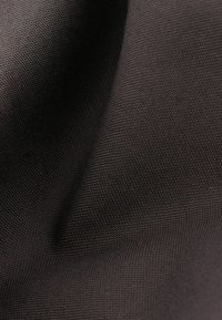 Gros plan d'un tissu texturé marron foncé avec un motif tissé et des plis doux créant profondeur et ombre.