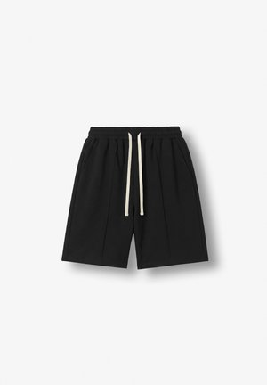 Shorts noirs longueur genou avec taille élastique et cordon blanc, avec poches latérales et un logo brodé discret sur la jambe droite.