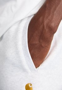Gray hoodie with a v-neck and a pocket, featuring a gold embroidered design. Close-up of a dark skin tone arm and textured fabric.