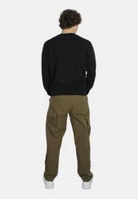 Felpa nera con colletto a girocollo, pantaloni cargo verde oliva con tasche laterali e sneakers bianche. Vista posteriore dell'outfit.