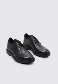 Chaussures en cuir noir avec une finition lisse, dotées d'un bout rond, de lacets à six œillets et d'une semelle en caoutchouc noir basse. Aucuns motifs ou accents visibles.