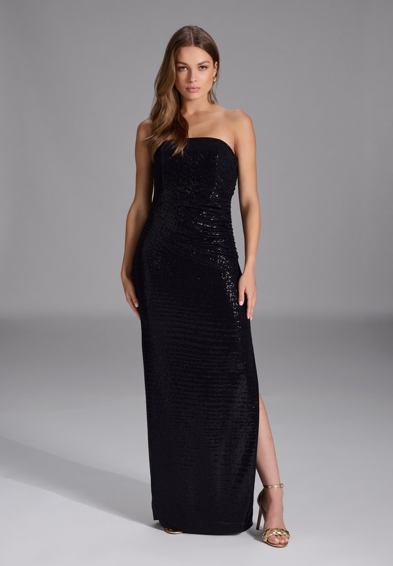 Abito da sera nero senza spalline con paillettes, silhouette aderente e spacco laterale. Indossato con sandali dorati con tacco alto. Tessuto a trama liscia.