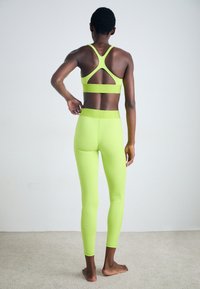 Neon žalia sportinė apranga, kurią sudaro strappy sportinė liemenėlė su iškirptu nugaros dizainu ir atitinkančios aukšto liemens elastinės kelnės. Lygus, elastingas audinys.