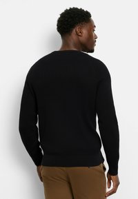 Schwarzer gestrickter Pullover mit einem strukturierten Muster, Rundhalsausschnitt und gerippten Bündchen. Besitzt eine taillierte Silhouette und einen Saum, der in der Taille sitzt.