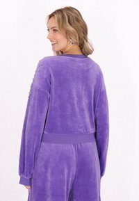 Bluza din velur mov cu un design scurtat, tiv cusut și umeri embellisați cu nasturi argintii. Textura moale și croiala lejeră.