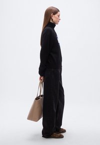 Pull noir à col roulé côtelé, jean noir à jambes larges, sac fourre-tout beige, et chaussures slip-on à imprimé léopard. Le modèle est présenté de profil.