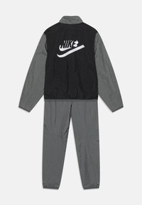 Nike trenirka u crnoj i sivoj boji. Jakna ima stojeći ovratnik i bijeli logo, dok su rukavi i struk elastični. Lagani materijal.