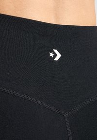 Černé sportovní legíny vyrobené z elastické tkaniny, s logem a detaily švů, se zblízka vyobrazeným pasem a texturou.