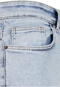 Tissu en denim bleu clair centré sur une poche arrière avec des coutures visibles et une boucle de ceinture en haut à droite.