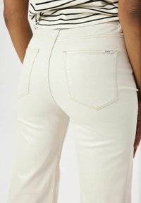 Crème-kleurige denim jeans met een aansluitend ontwerp, voorzien van twee achterzakken en subtiele stikdetails. Een gladde textuur over de hele lengte.