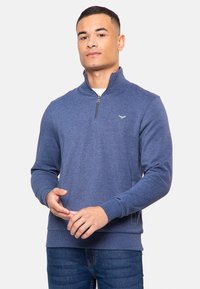 Sudadera de color azul marino hecha de tejido suave, con cremallera de cuarto, puños acanalados y un pequeño logotipo en el pecho.