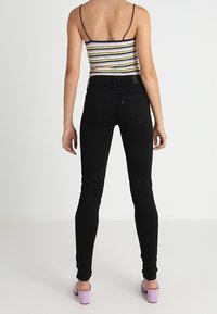 Jeans ajustados negros de cintura alta, con una textura suave y un diseño clásico de cinco bolsillos. Combinados con una camiseta sin mangas a rayas y tacones morados.